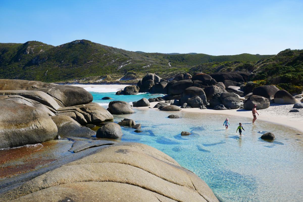 children wading through the sheltered waters between granite boulders and the beach