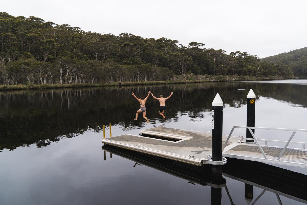 Two people jumping off a jetty into water. 