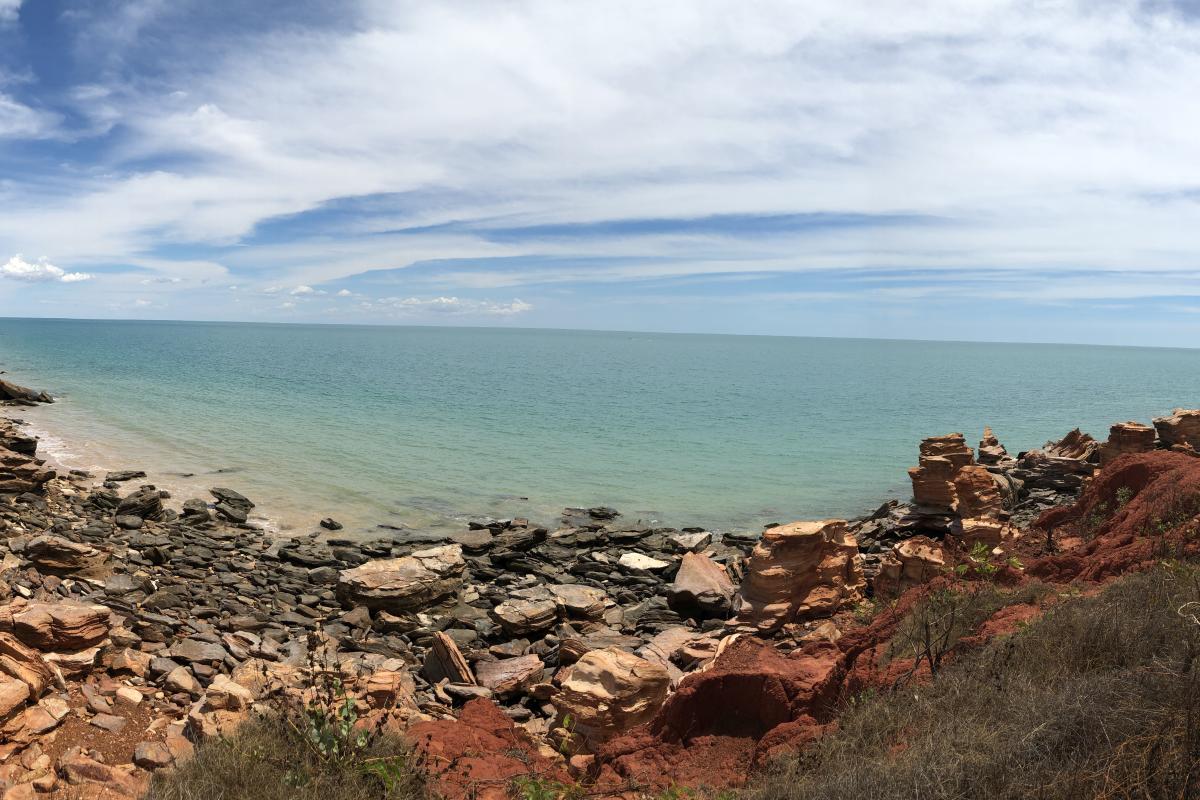 Red rocks and cliffs leading to green blue waters. 