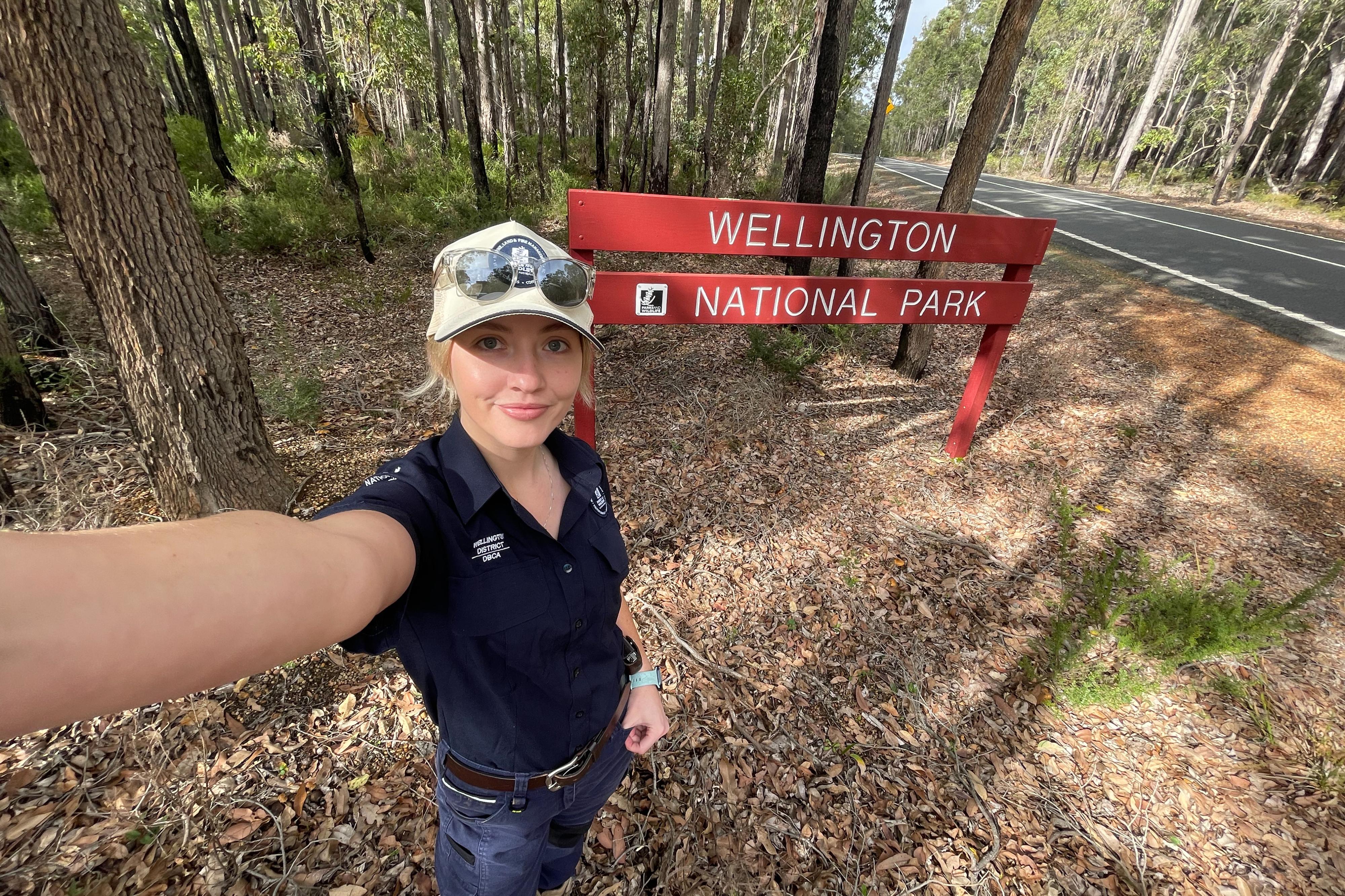 Person holding camera taking a selfie next to a sign. 