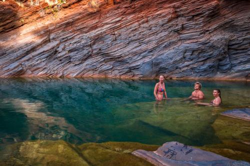People sitting in a natural pool of clear green water surrounded by walls of layered red rock