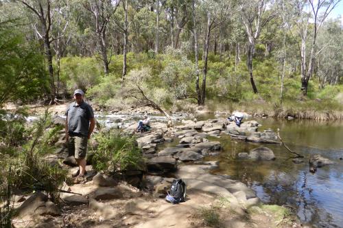 two hikers resting by a gently flowing stream in a native forest