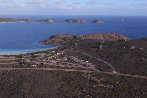 aerial view of a coastal campground and camp sites adjacent to a curved bay with blue sea and light clouds