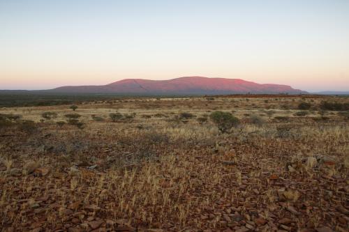 a vast open outback plain with a huge granite rock mountain towering in the distance