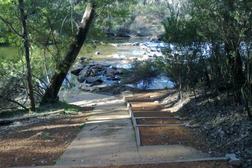 man made ramp leading down to a wide rock strewn brook in a native forest