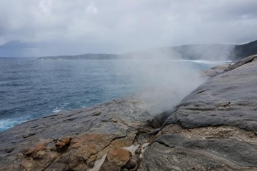 Blowholes with spray and a view of the ocean and coastline to the west in the background