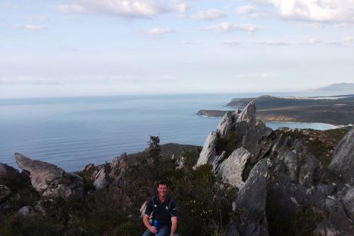 man at East Mount Barren with a view of the coastal landscape and expanse of blue ocean in the distance