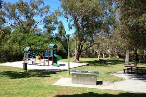 Childrens play equipment and barbecues with shady trees beside the river