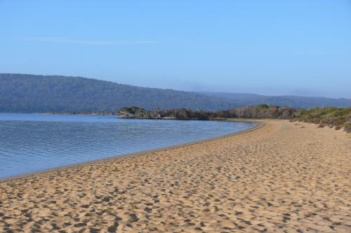 sandy beach of the still waters of the inlet with blue skies and low hills in the distance