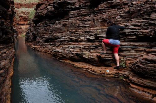 Person walking and climbing on rock wall above water 