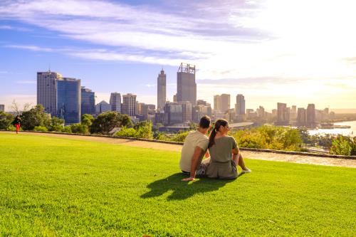 Two people sitting on the lawn looking at the Perth city skyline.