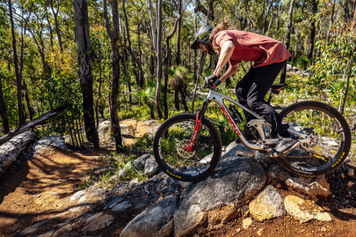 Person riding mountain bike on rocks near a trail. 