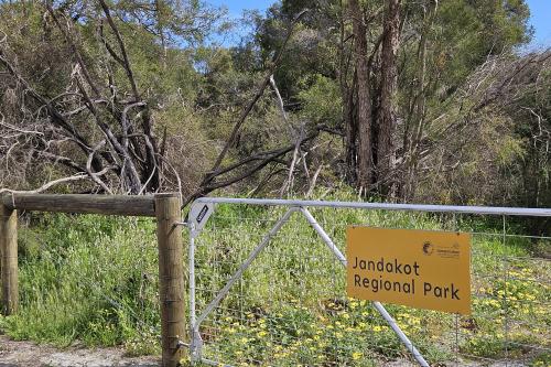 Metal wire fence with orange sign and bush. 