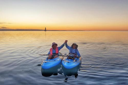 Twop people sitting in kayaks in the ocean with the sun set behind them.