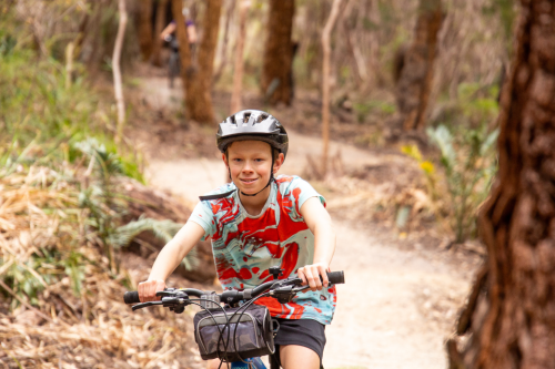Close up of person smiling at the camera while riding a bike on a trail. 
