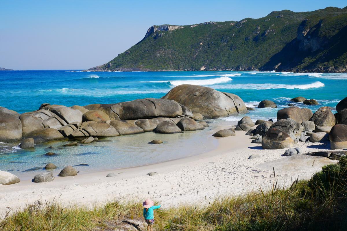 view of headland with beach in front white capped waves rolling in and child playing in sand