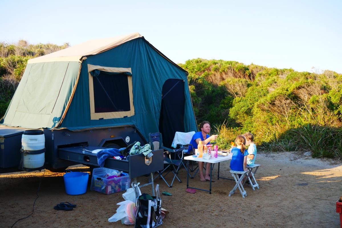 camper trailer set up with adult and children sitting in campig chairs