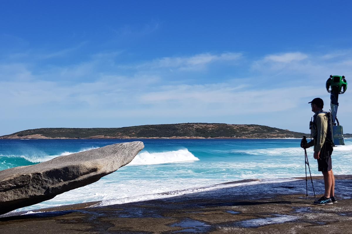 Cape Arid National Park blue ocean with white capped waves and a man standing on the shore wearing a backpack with a camera ball