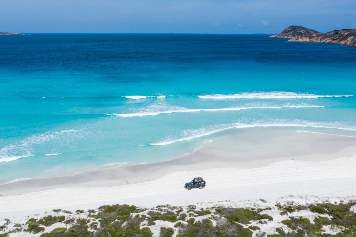 Lucky Bay four wheel drive on white sandy beach next to bright blue water