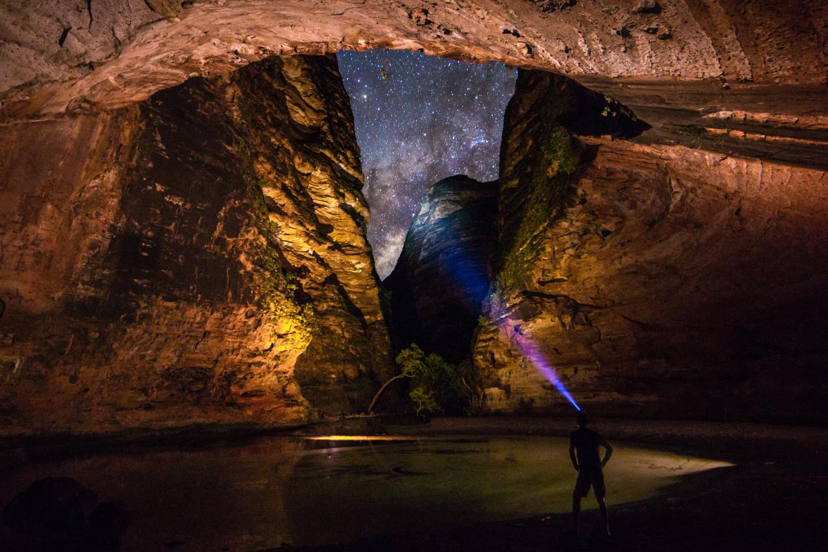 man standing in dark with head torch surrounded by walls of rock