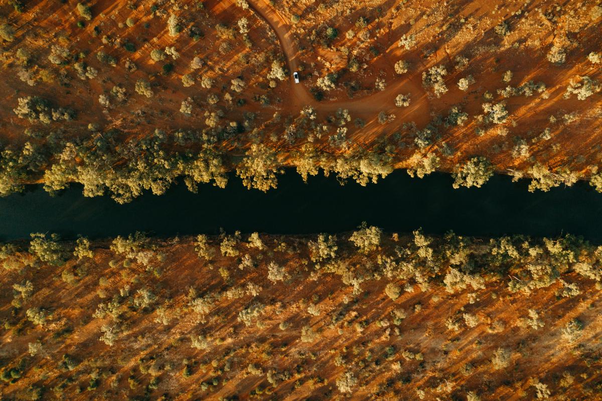 aerial view of outback river with water outback trees and a vehicle driving on a red dirt track