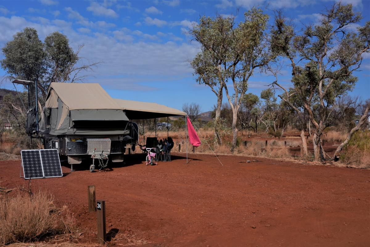 Camper trailer on red dirt with few trees and blue skies