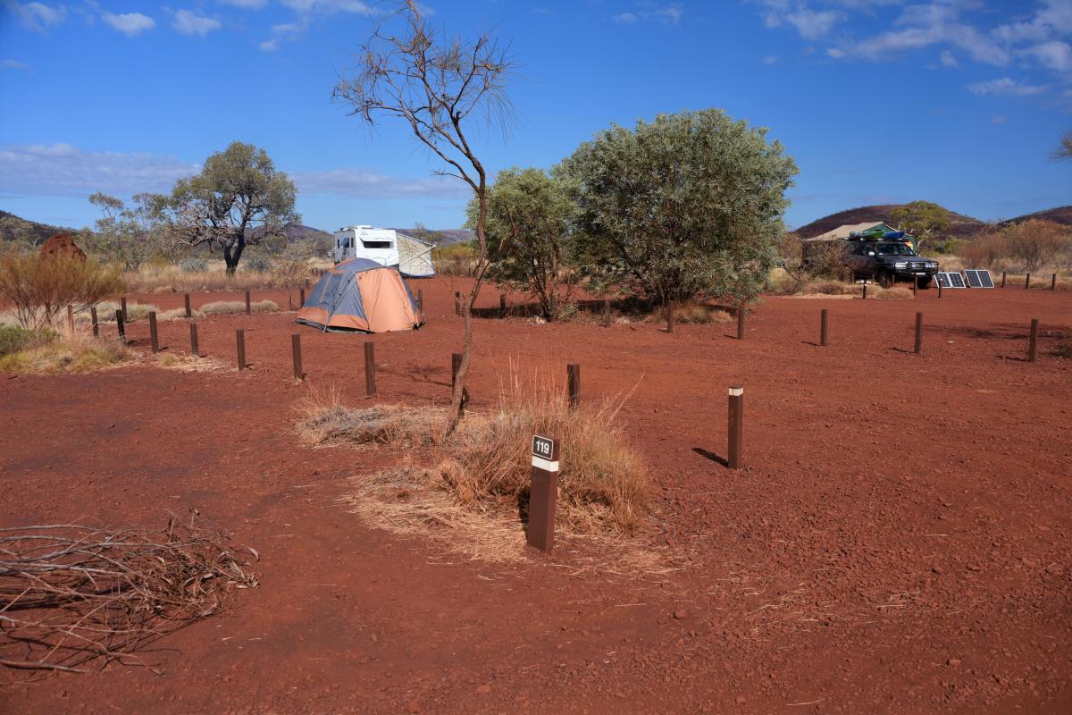 Tents and caravans on red dirt with trees and blue skies