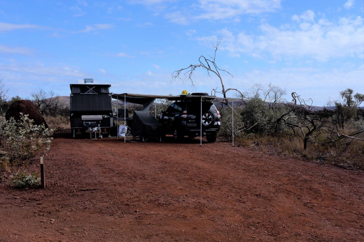 caravan and vehicle with tarp shelter on red dirt with low vegetation and blue skies