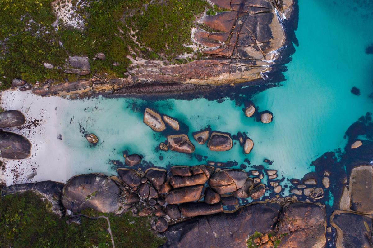 aerial view of green water surrounding large granite boulders 