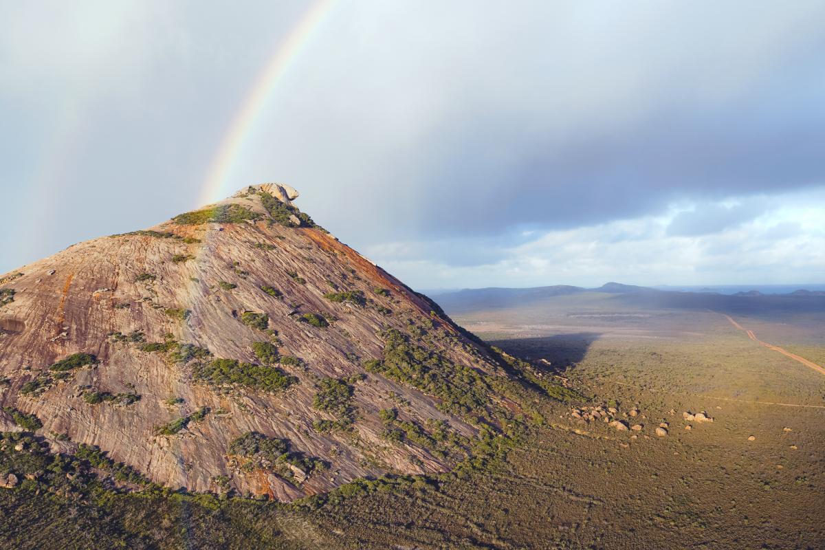 large rocky hill with grey clouds and rainbow