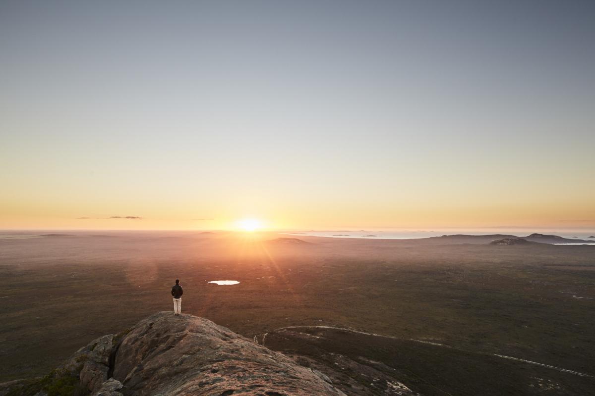 person standing on rock looking out at sunset