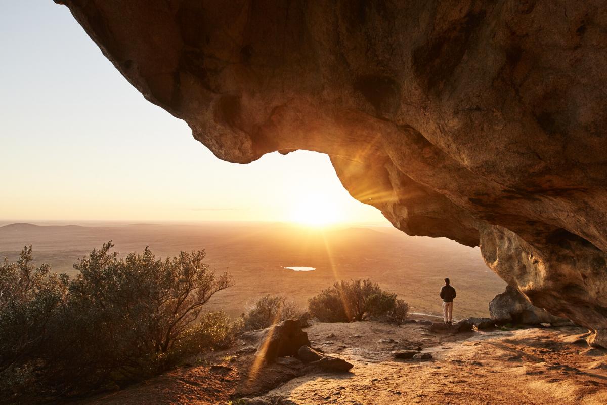 man standing under rocky outcrop with sunset