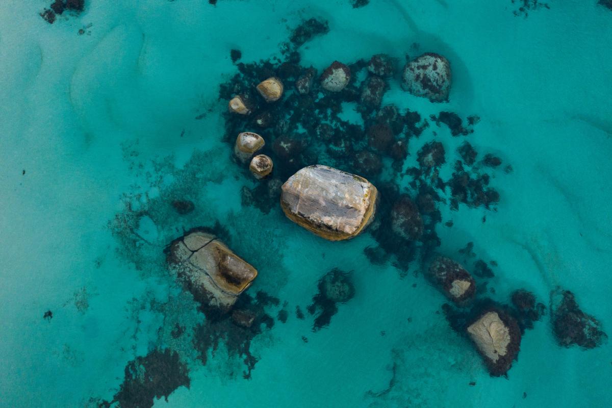aerial view of clear green water surrounding large granite boulders