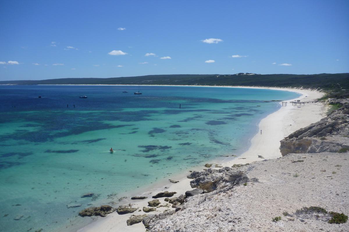 sweeping sandy bay with turquoise still waters and a couple of boats anchored