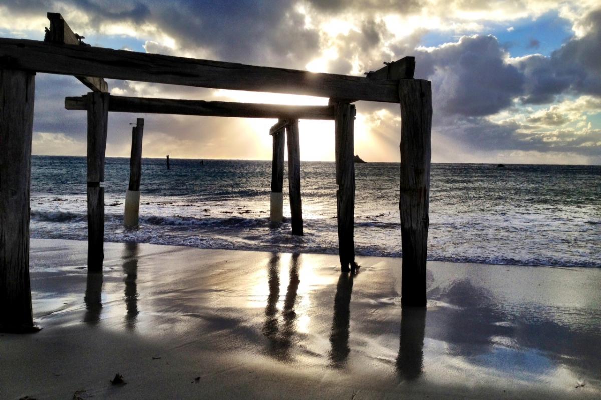 remnants of a wooden jetty beside the ocean with a cloudy sunset in the background