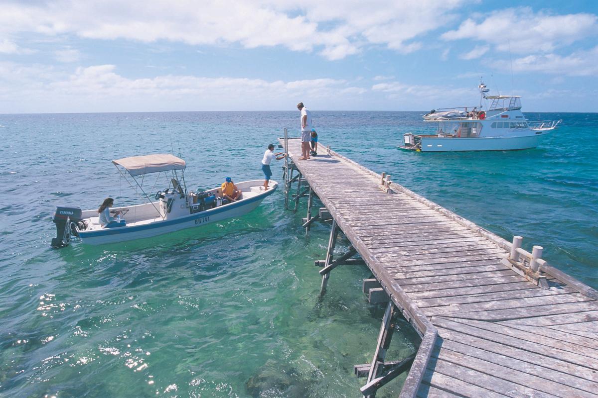 Houtman Abrolhos Islands National Park wood jetty over clear blue water with people in a small boat