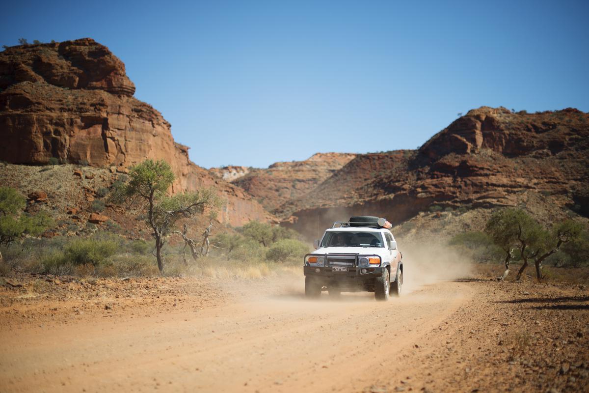 four-wheel drive vehicle driving on dirt road with large rock hills in the background