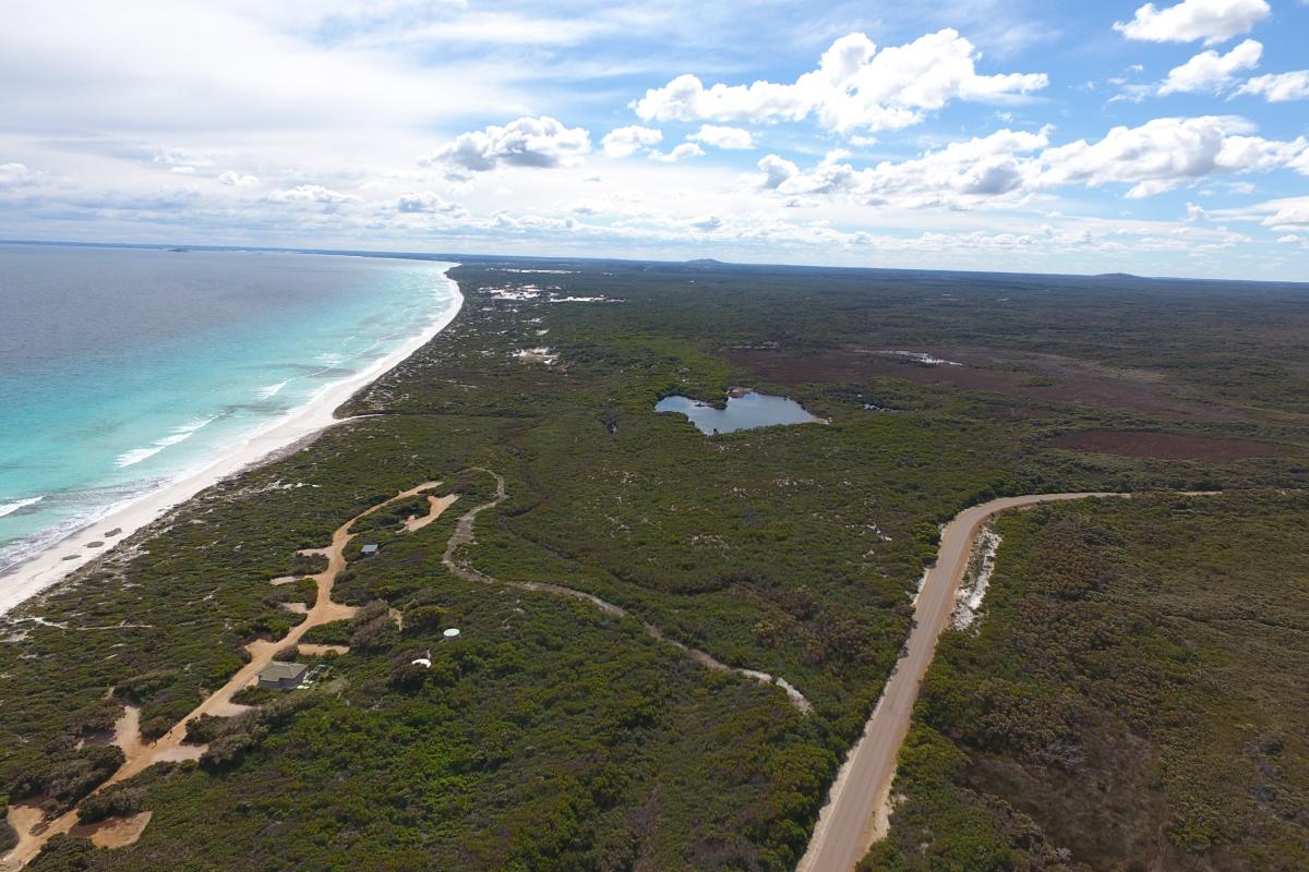 aerial view of a coastal road with camping sites adjacent to a long sandy beach with blue sea and light clouds