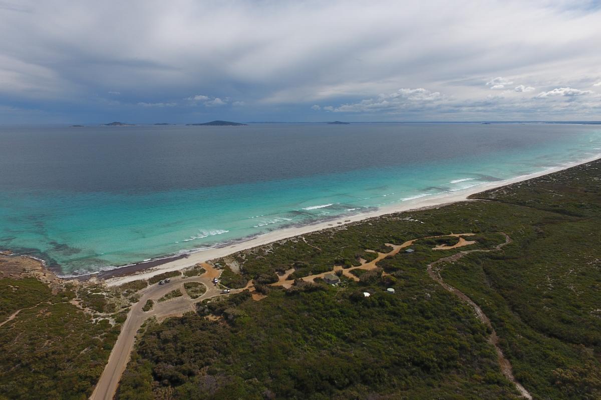 aerial view of a coastal campground and camp sites adjacent to a long sandy beach with blue sea and light clouds