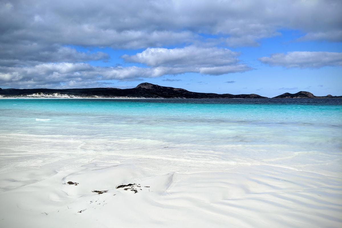 White sand and clear turquoise water of Lucky Bay beneath a cloudy sky