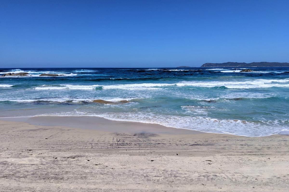 The eastern end of Mazzoletti Beach near Greens Pool, with a view towards Point Hillier Blue water with granite rocks and waves crashing, and a distant view of Point Hillier