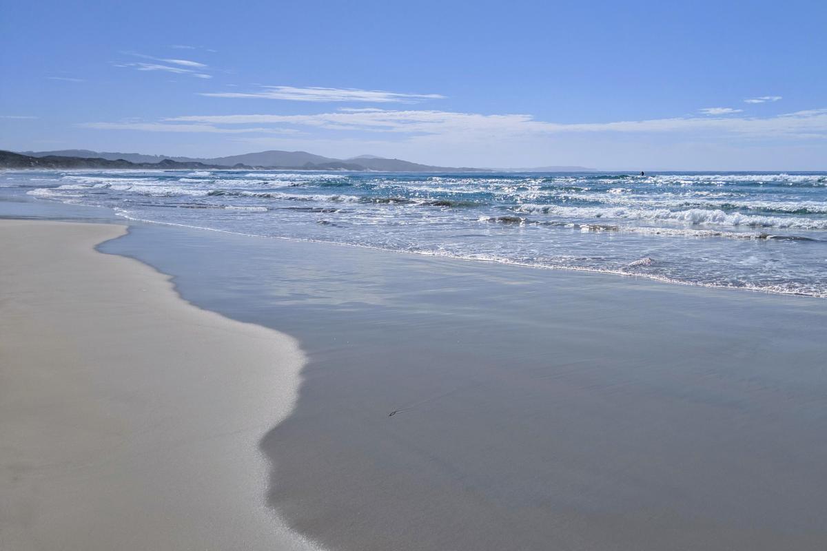 Long beach with small waves, and hills in the far distance