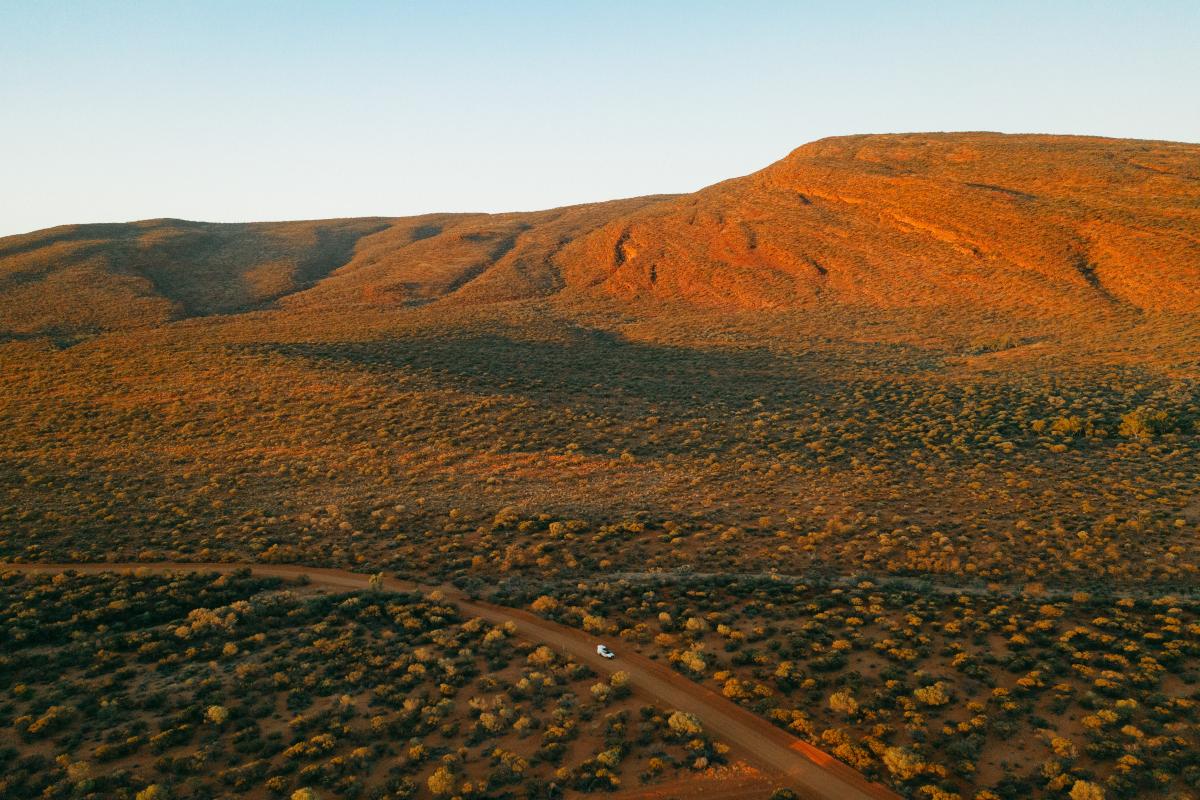 aerial view of a lone vehicle travelling on a dirt road in a rugged outback landscape 