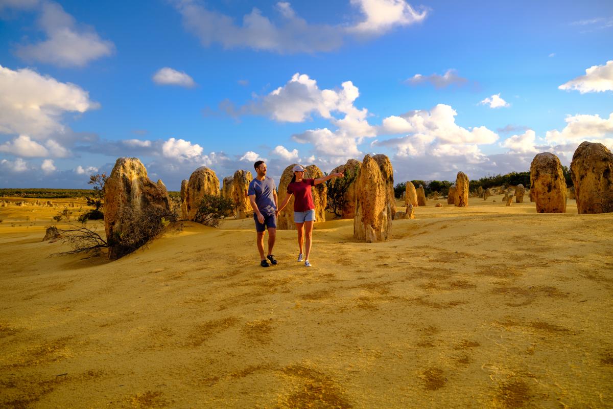 two people standing on yellow sand surrounded by tall yellow rock structures coming up from the sand