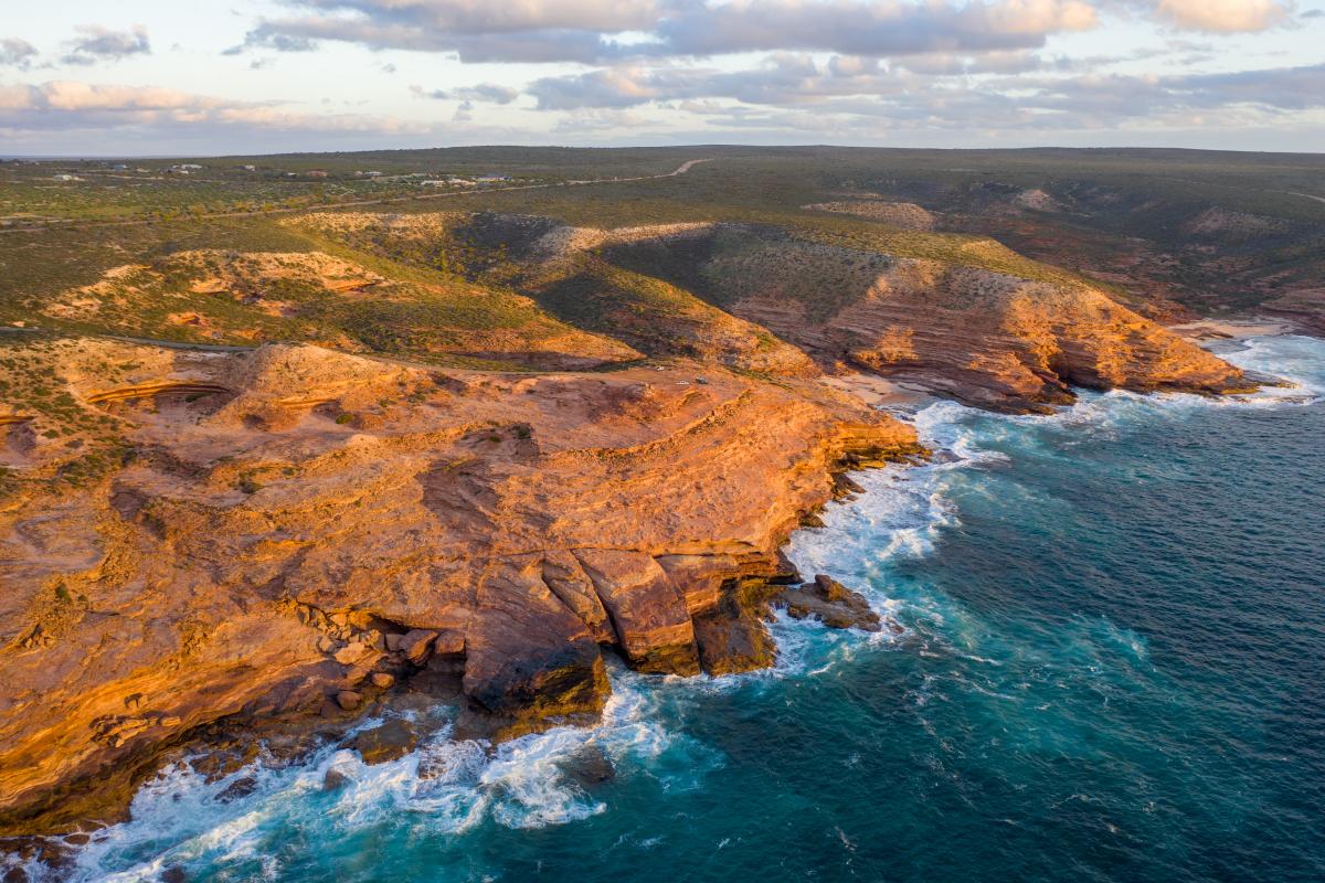 Aerial view of rugged coastline at sunset showing turquoise water against the luminescent red rock.