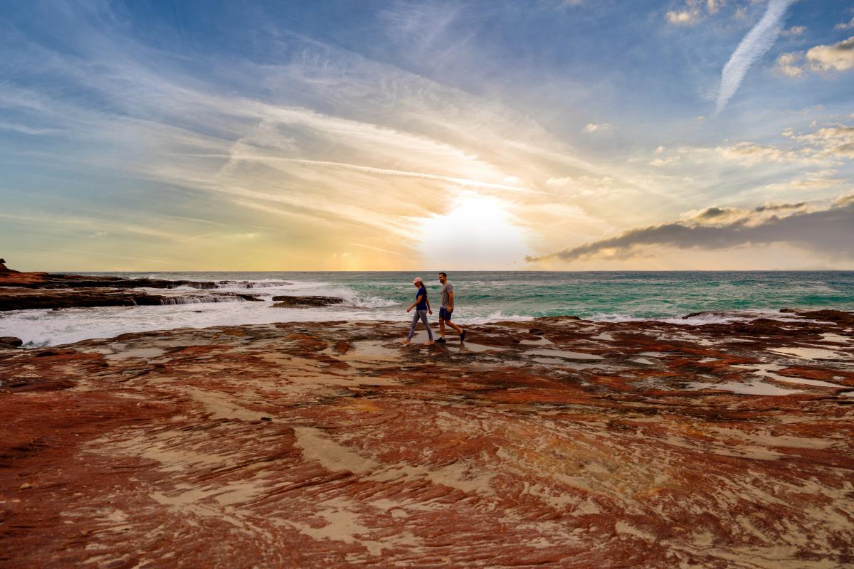 Couple walking on red rocks at beach at sunset