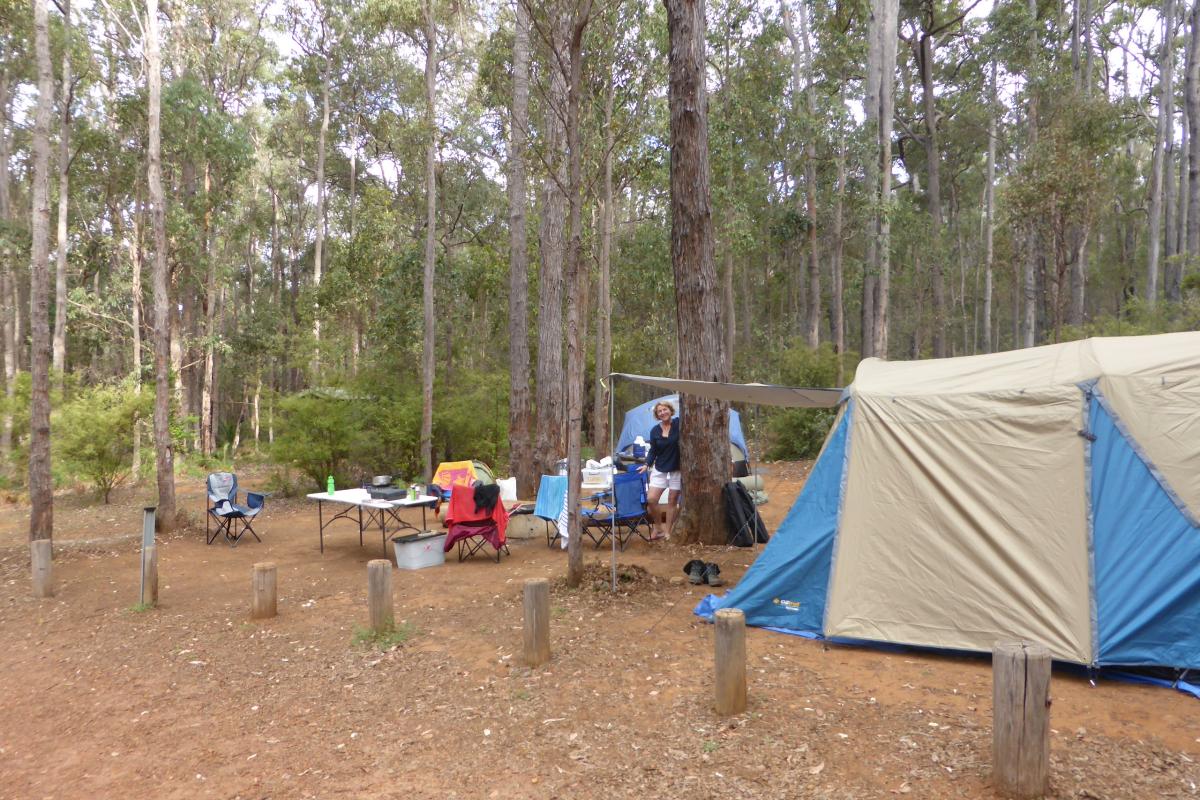 a lady at her campsite with large tent and camping table and chairs