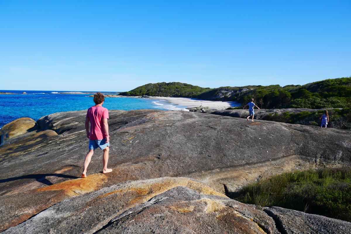 people walking on large granite rocks next to beach with blue water