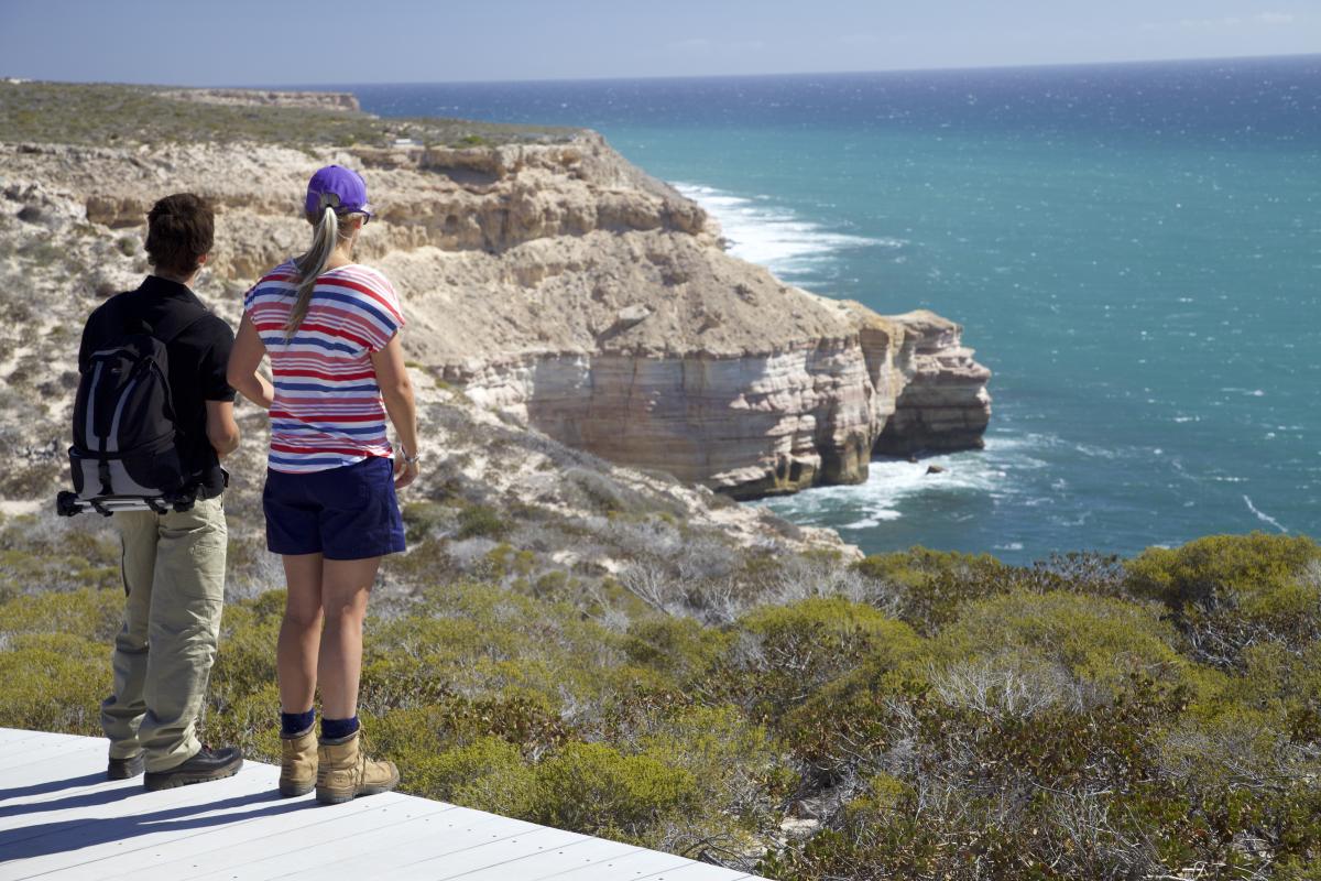 two people on a trail looking over the rugged coastline and the blue ocean