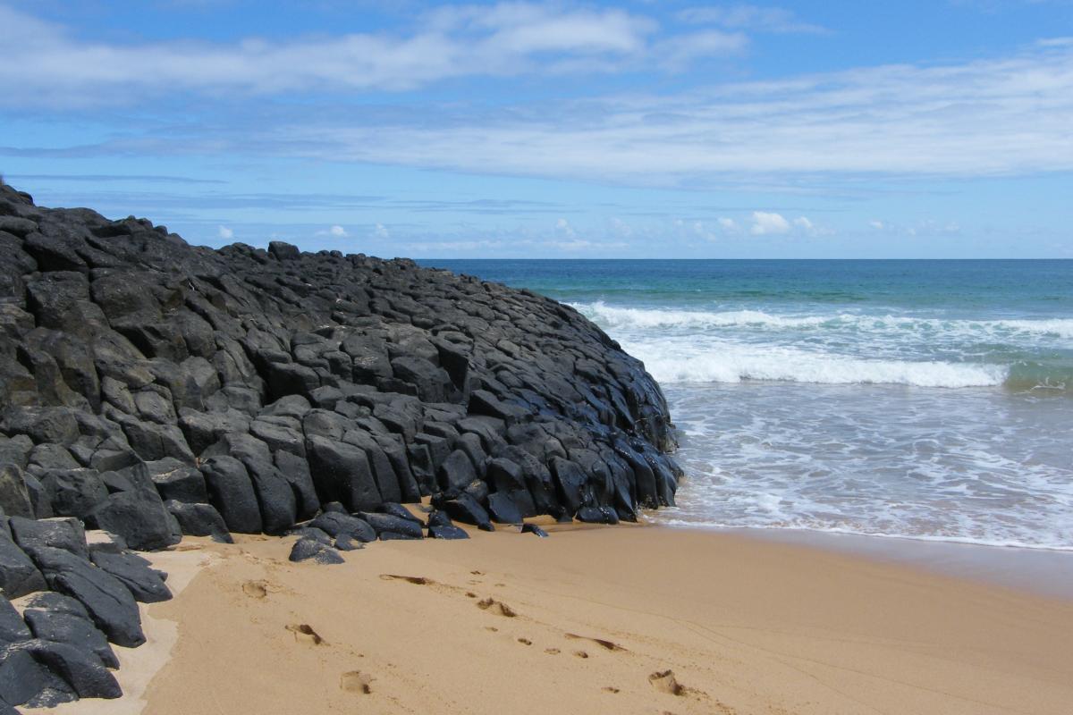 footprints in the sand leading up to black rocks and ocean waves 